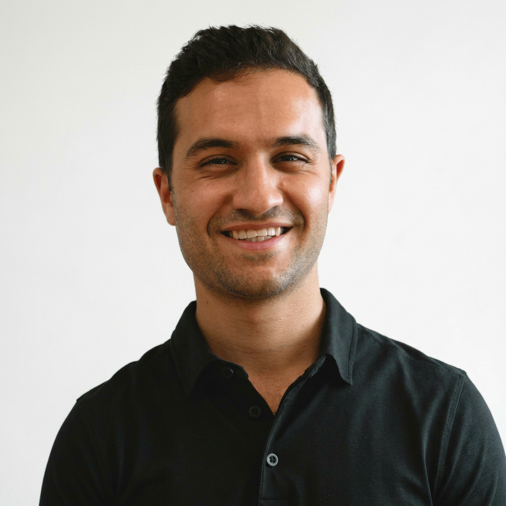 A smiling man with short dark hair wearing a black collared shirt against a plain white background.