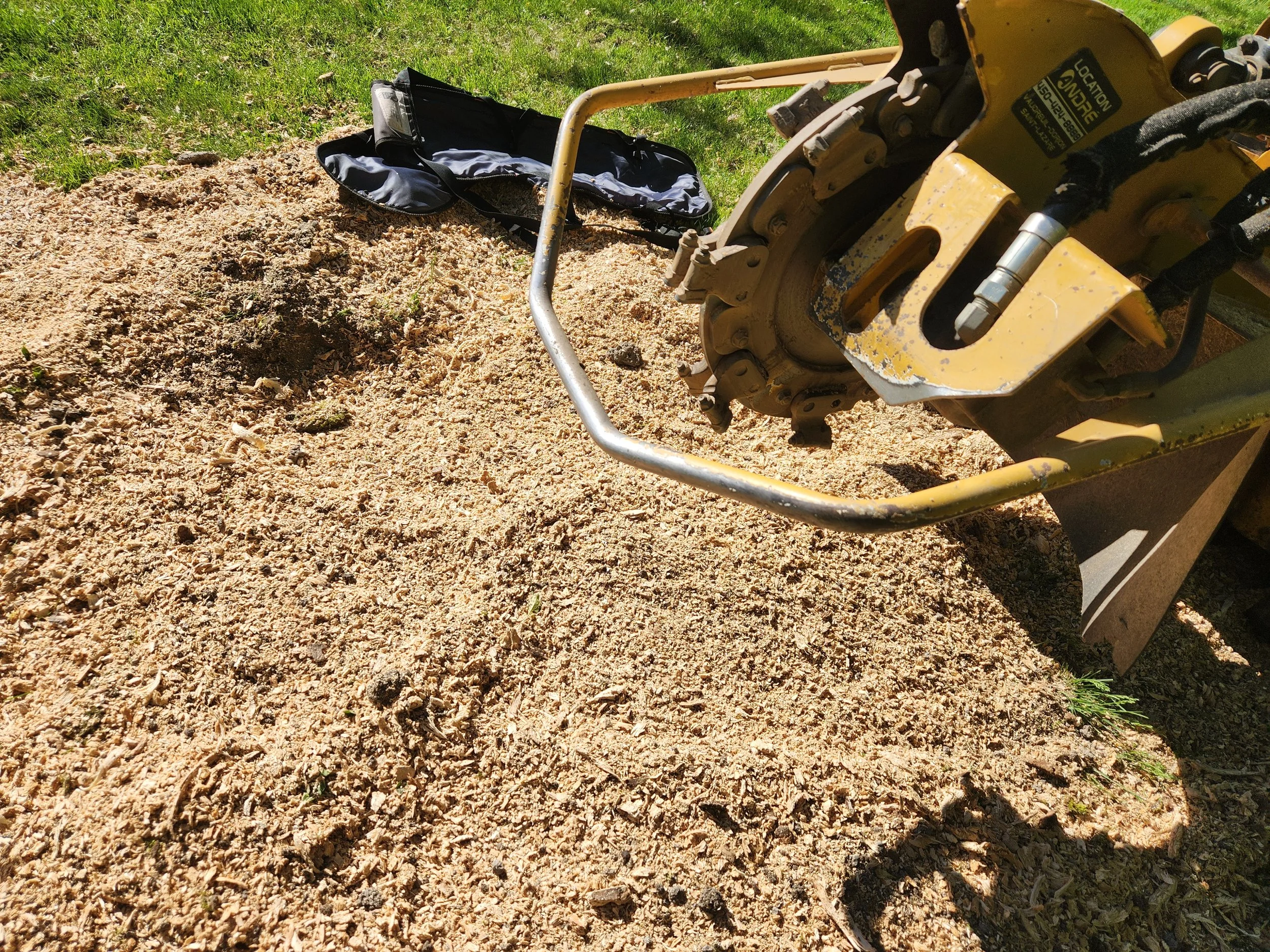 Close-up view of a yellow construction compactor machine with a gravel and dirt surface in front of it, on a grassy outdoor area.