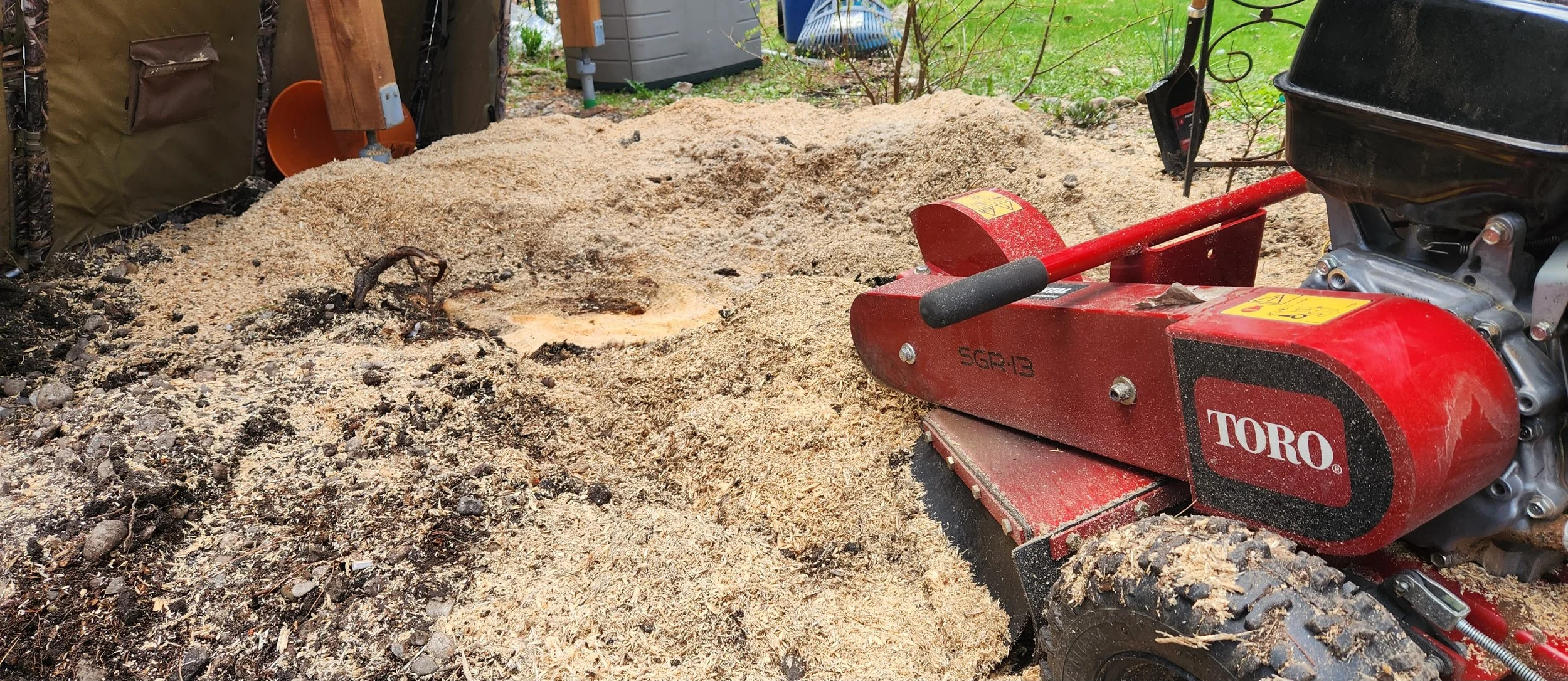 A red wood chipper machine outdoors with wood chips and debris around it.