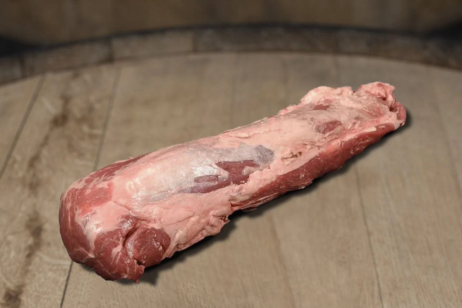 Raw piece of meat, possibly a beef or pork cut, lying on a tiled wooden floor.