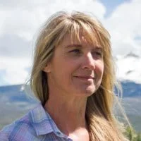 Jerilyn Nieslank standing outdoors in front of a mountain landscape and cloudy sky.