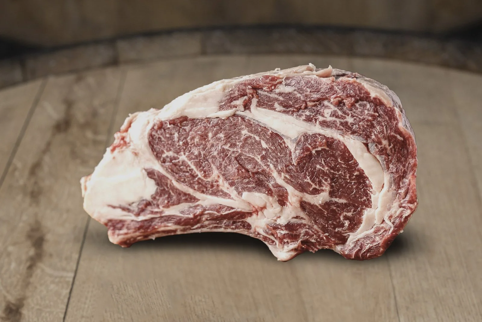 A large, raw cut of marbled beef steak on a wooden surface.