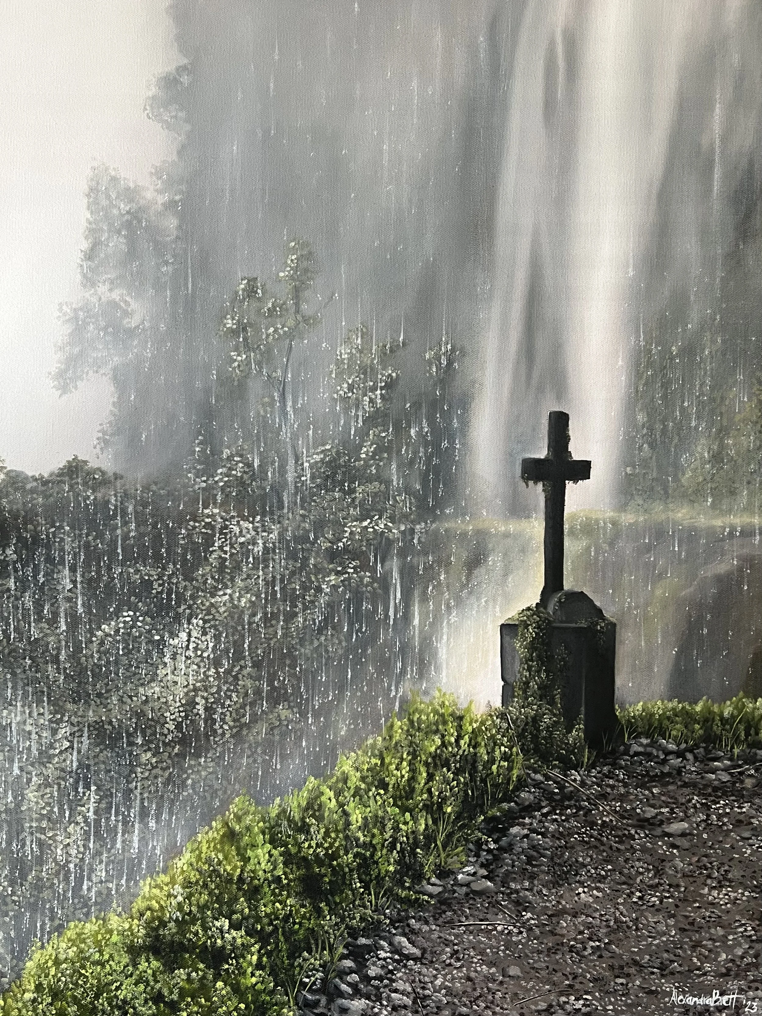 A cross monument near a rushing waterfall in a forest with lush green plants and rocks in the foreground.