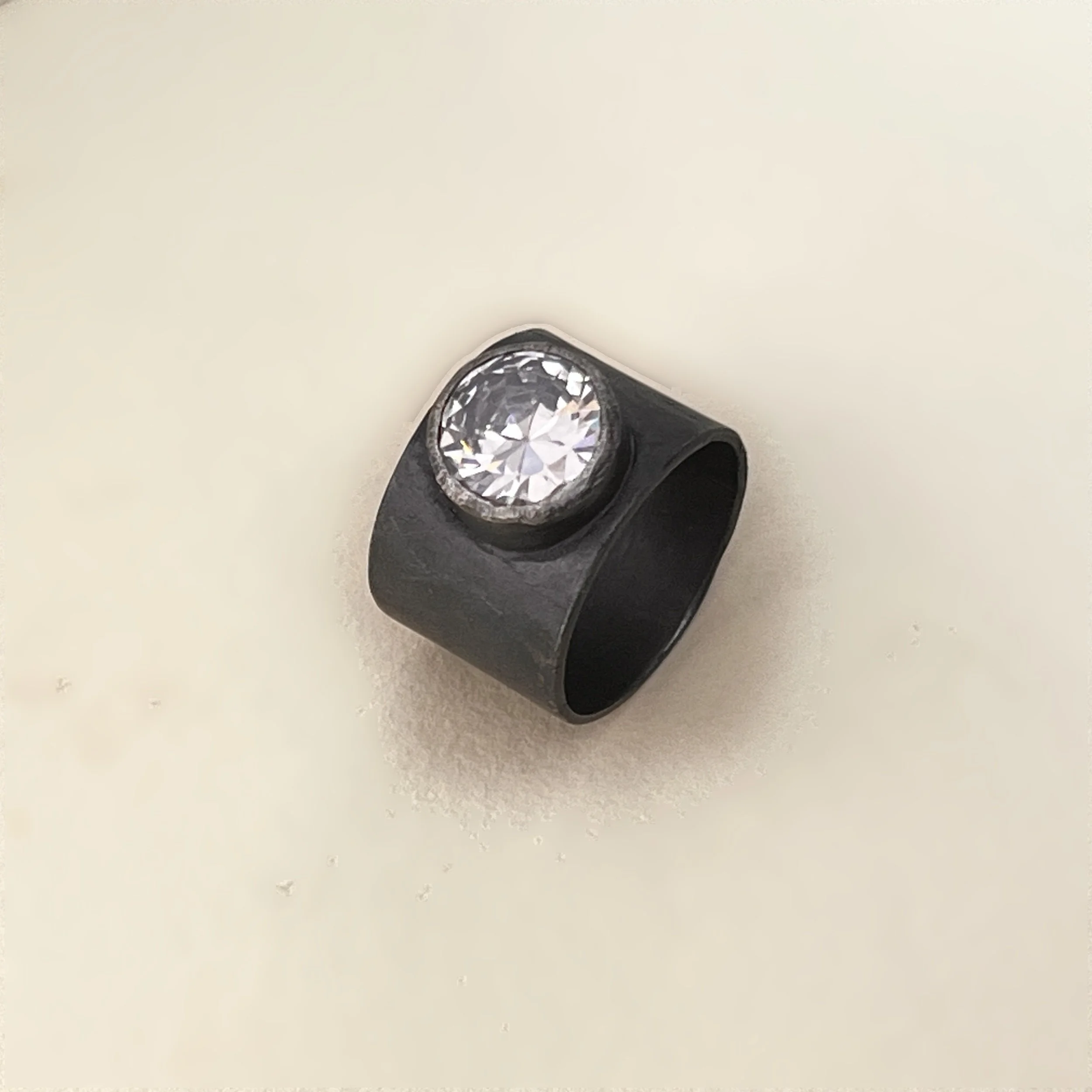 Cigar band ring — round faceted cubic zirconia set in oxidized sterling silver.
Band 15mm · thickness 1mm · stone 11mm