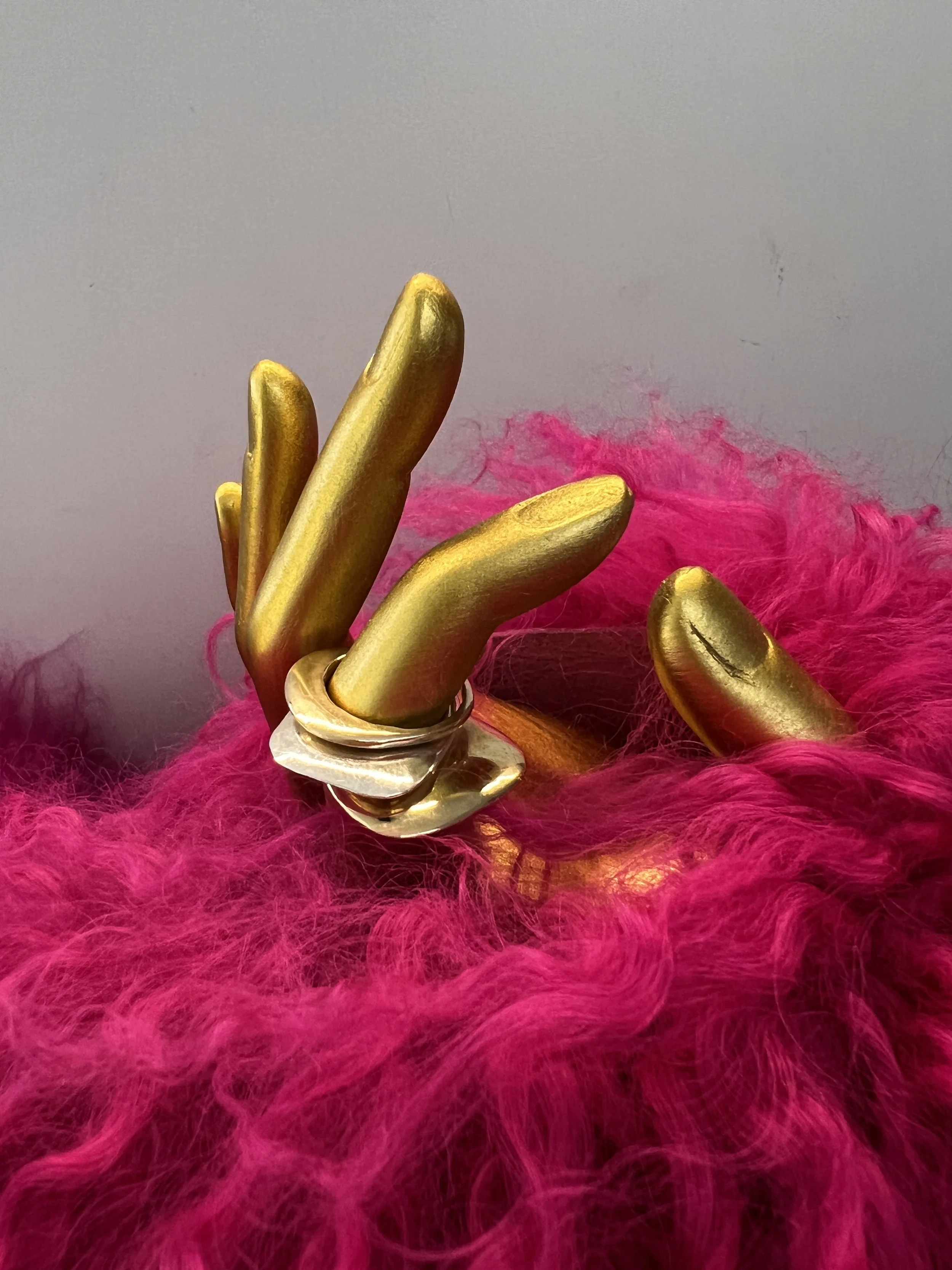 gold, silver and brass stacking rings on gold hand with pink fur background