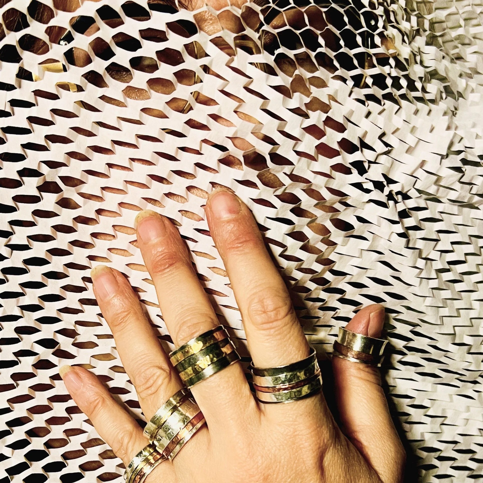 Person's hand wearing multiple rings with a honeycomb or textured pattern, fingers touching a patterned, perforated surface.