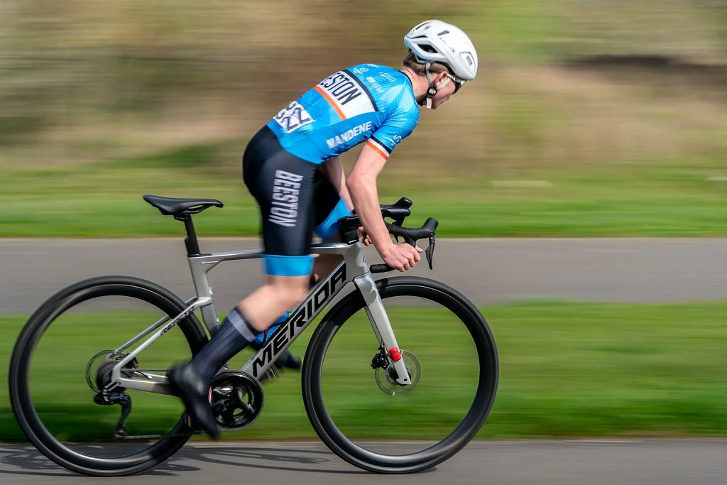 A cyclist in a blue and black uniform riding a silver Merida road bike on a paved path.