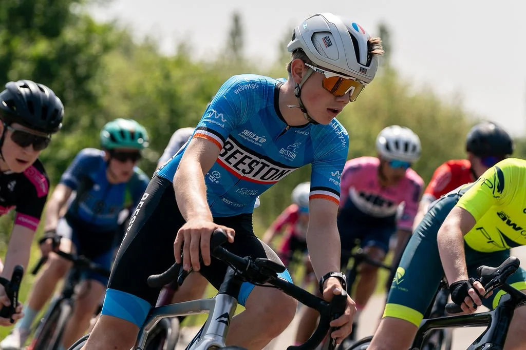 Group of cyclists racing outdoors, wearing colorful jerseys and helmets, with a focus on a cyclist in a blue jersey riding a mountain bike.