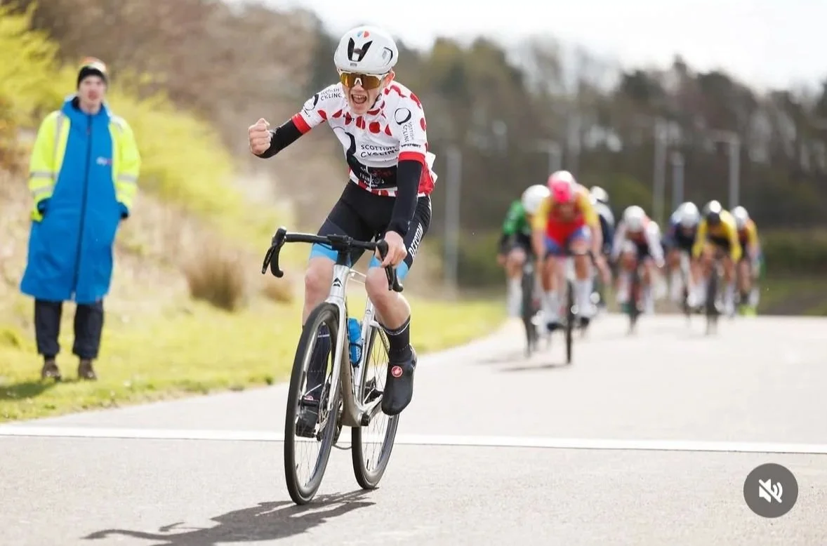 A cyclist in a white and red jersey celebrates as they cross the finish line ahead of a group of racers during a cycling race.