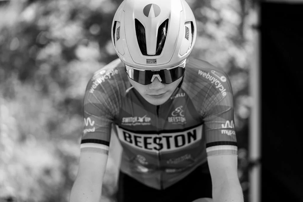 A cyclist in a Beeston team jersey wearing a full face helmet and sunglasses, in a cycling race.