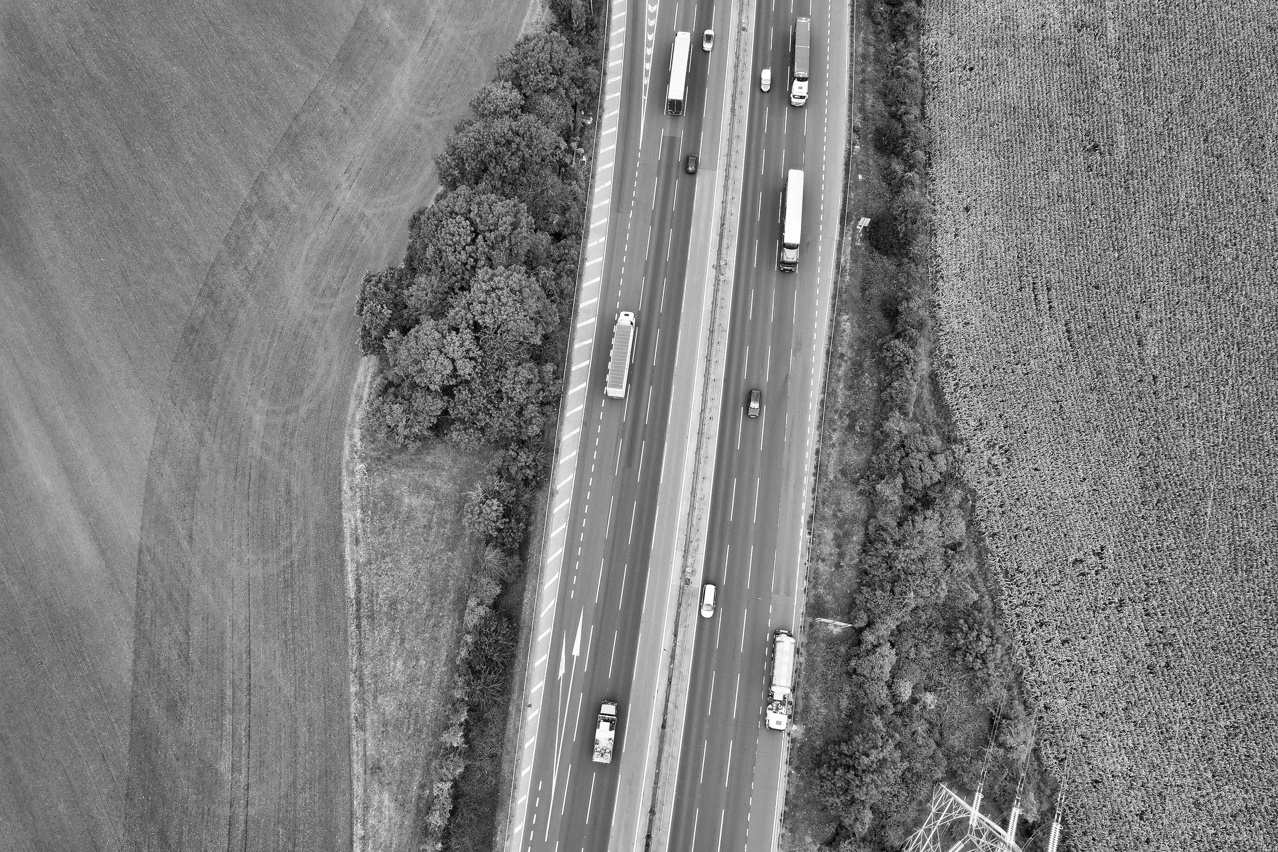 Aerial view of a highway with cars and trucks, flanked by fields and trees on both sides.