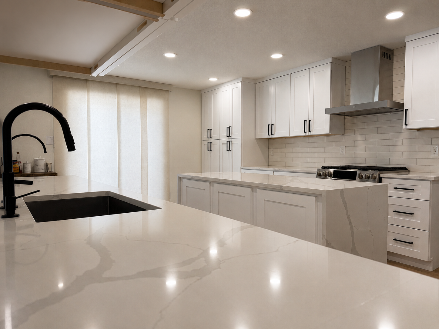 Modern white kitchen with marble countertops, black faucet, and stainless steel appliances, including a vent hood and gas stove.