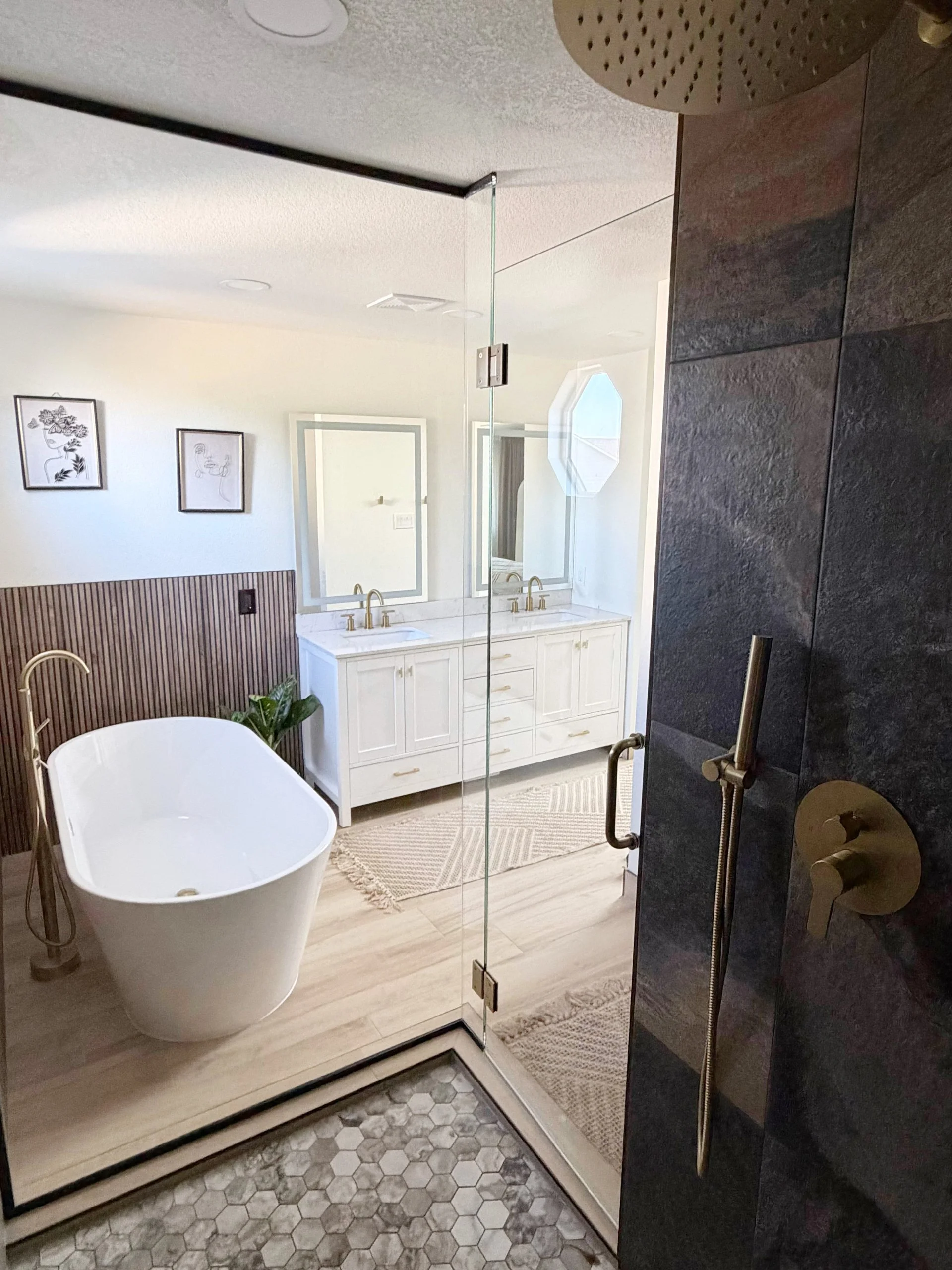 Finished primary bathroom viewed through the glass shower, with a freestanding tub, white vanity, and wood accent wall.