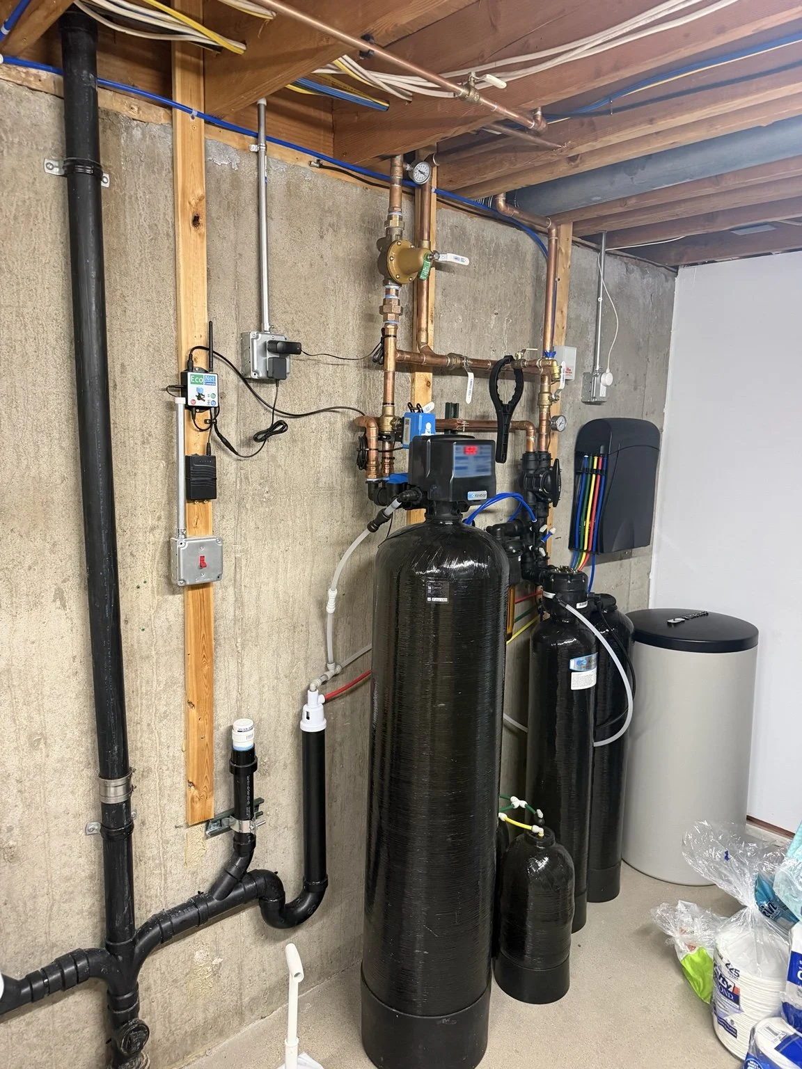 Water treatment equipment with multiple tanks, copper piping, valves, and controls in a basement utility area.