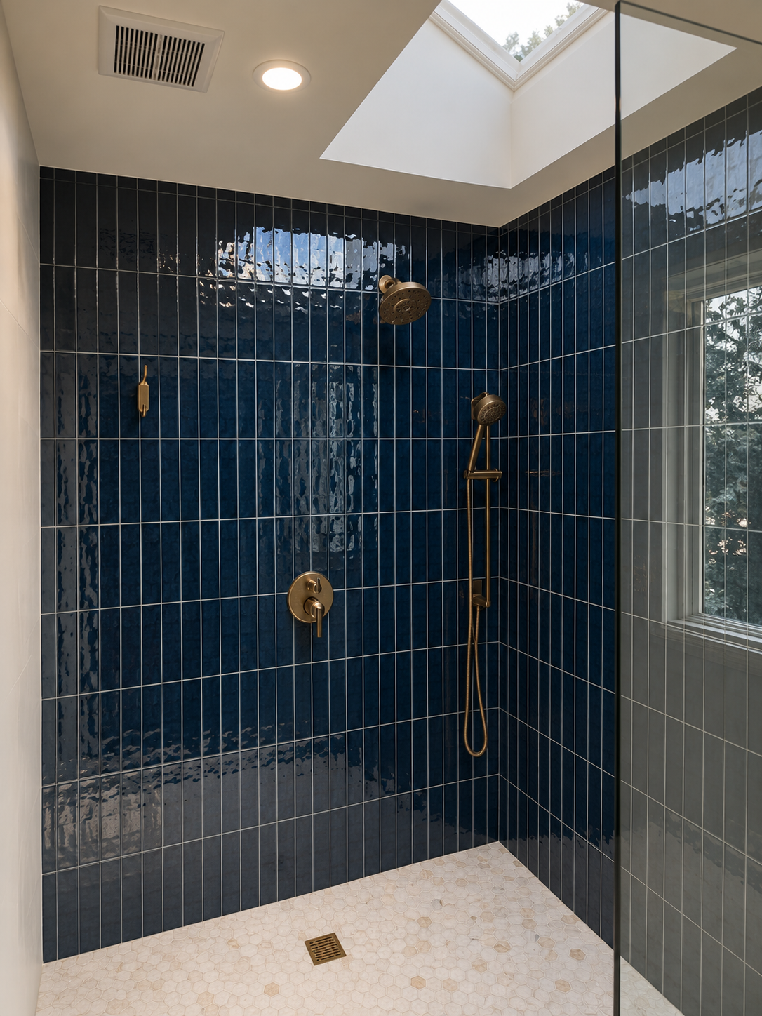 Modern shower with navy blue tiled walls, brass fixtures, a rain showerhead, a handheld showerhead, a skylight, and a window with natural light.