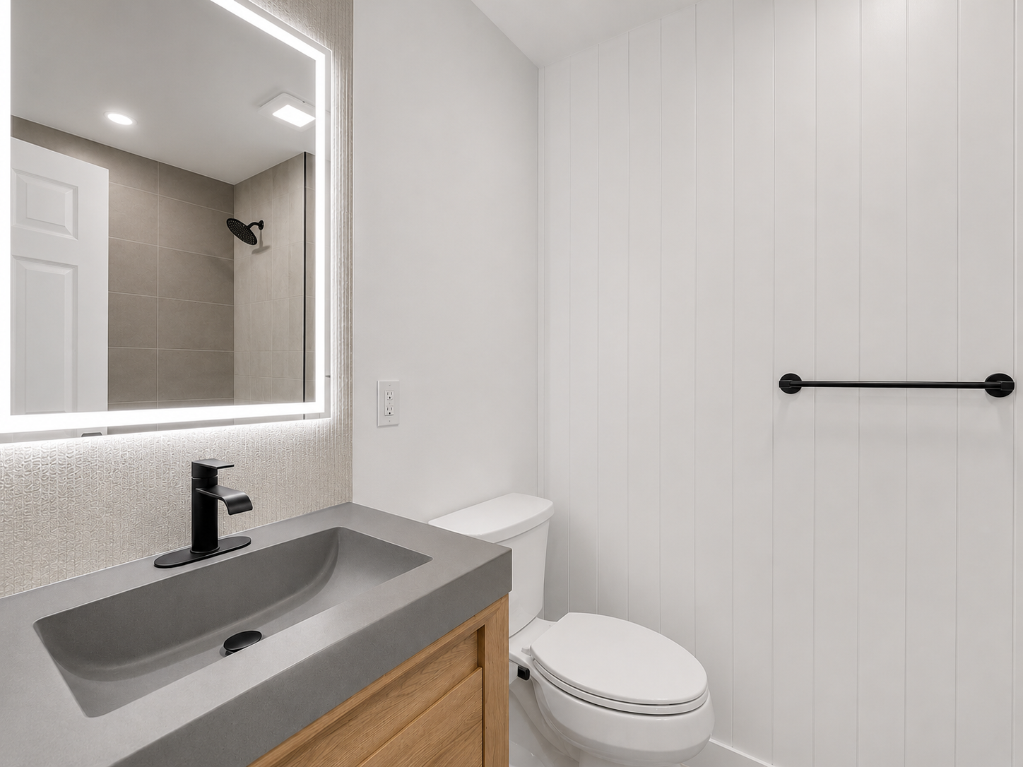Modern bathroom with white walls, a gray vanity with a black faucet, a large backlit mirror, a toilet, and a walk-in shower with beige tiles and a black showerhead.