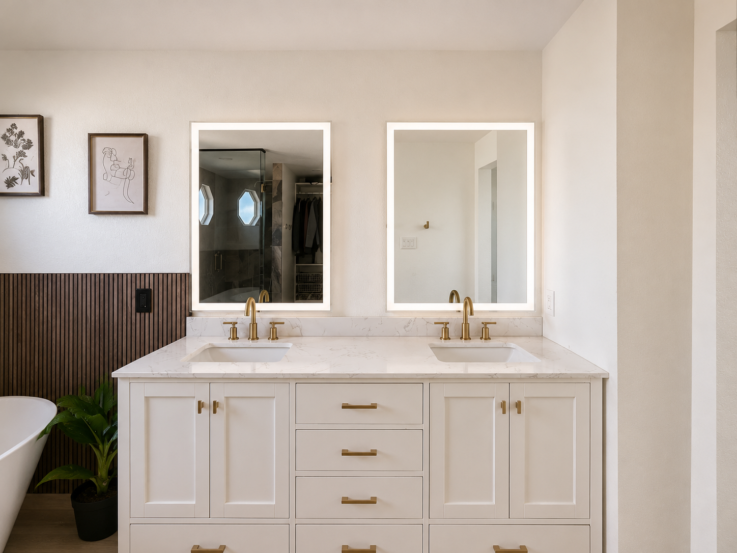 A modern bathroom vanity with a white countertop, two sinks, and gold fixtures. Two illuminated mirrors are mounted above the vanity. In the mirror reflection, a walk-in shower with glass doors and a walk-in closet are visible.