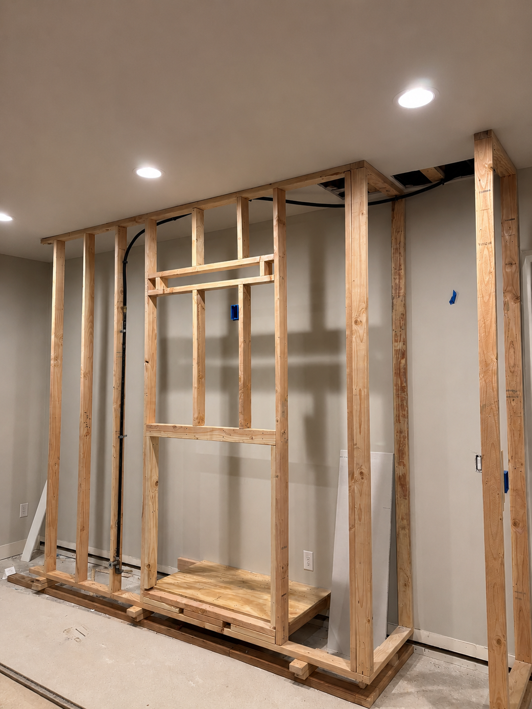 Construction of a wooden wall frame with exposed studs and wiring in a room.