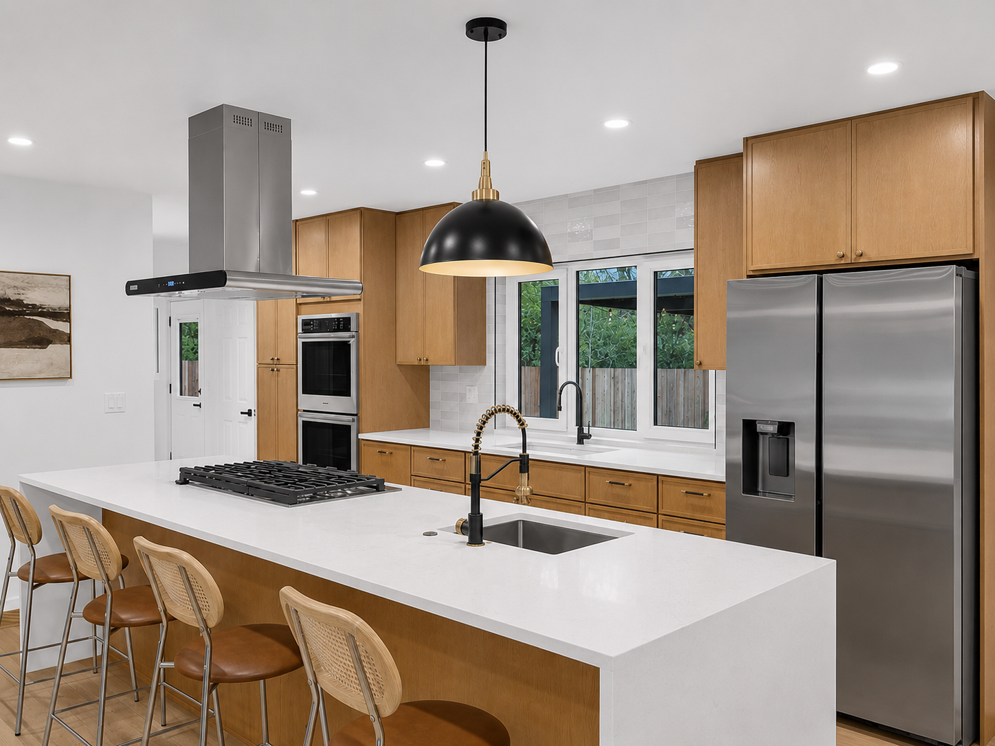 Modern kitchen with a white island and wooden cabinets, stainless steel refrigerator, double oven, black range hood, and black pendant light, viewed from the living area.