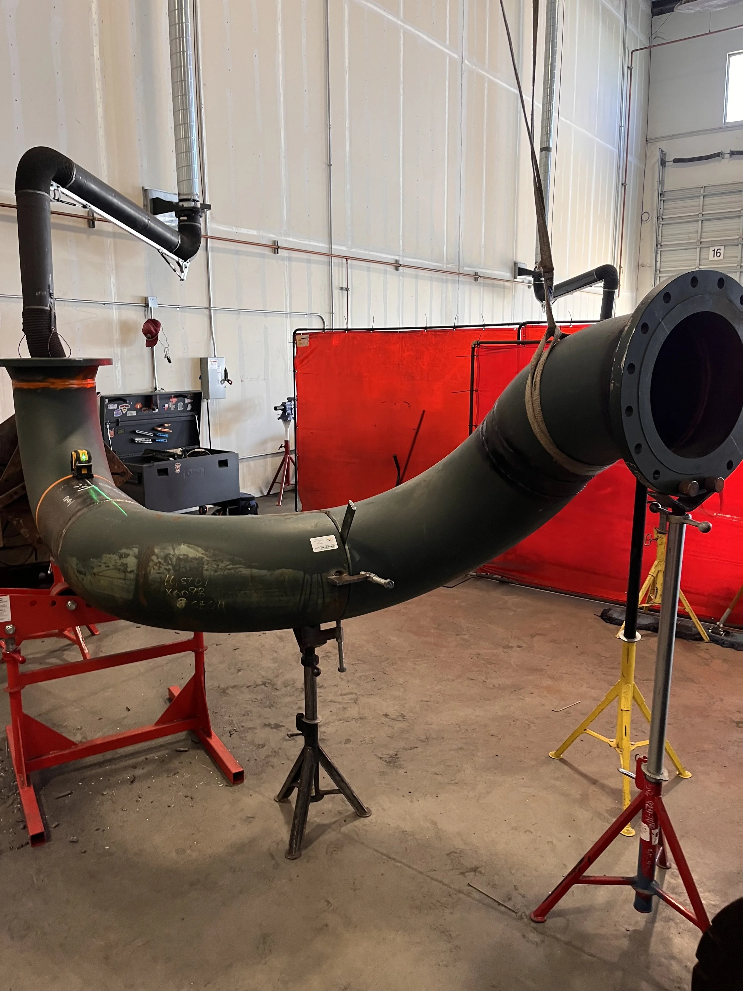 Industrial workshop with large pipe structure, various tools, a red partition, and equipment on stands, inside a warehouse.