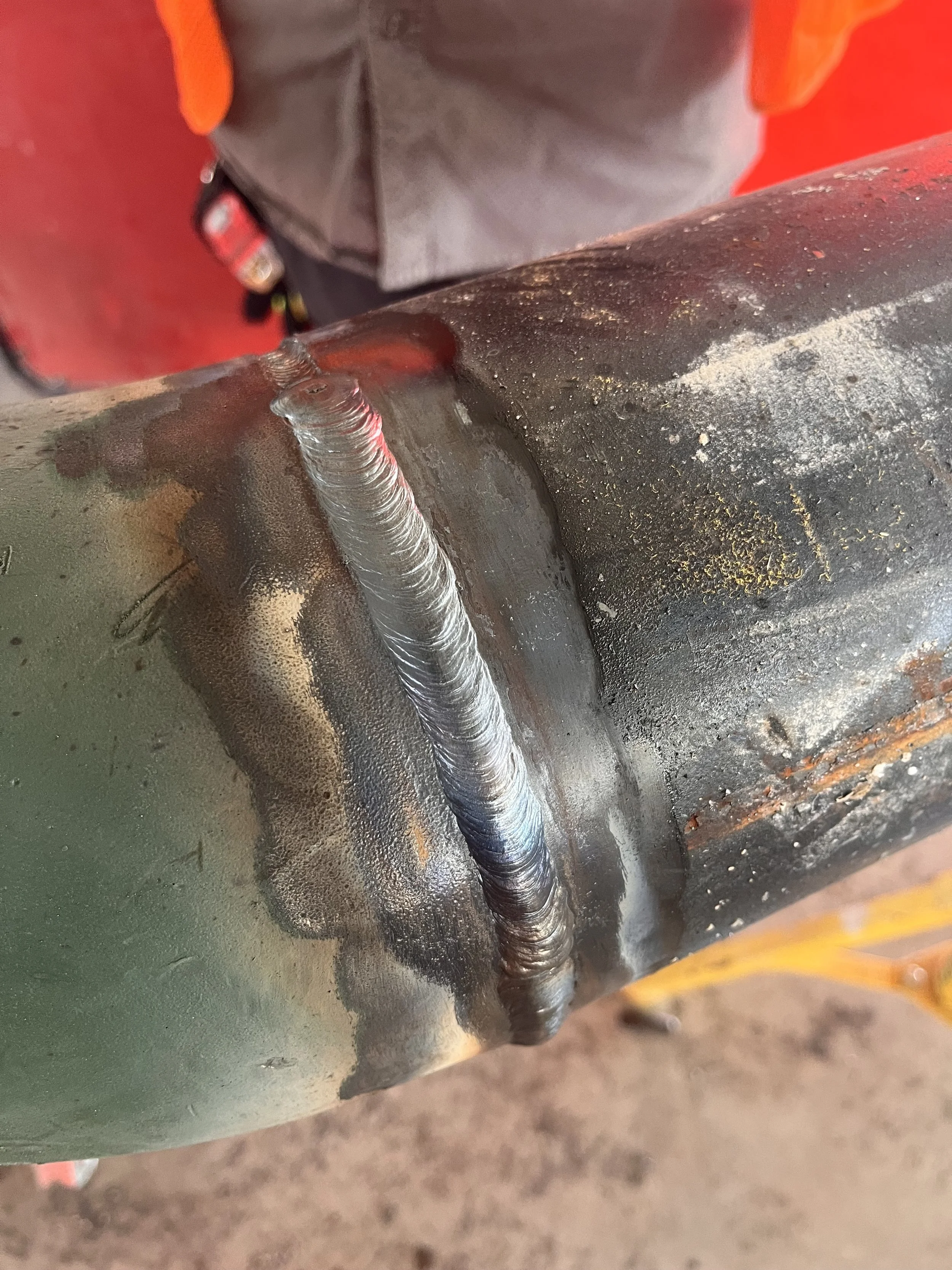 Close-up of a metal pipe or component with a weld bead, showing some discoloration and rust on the surface.