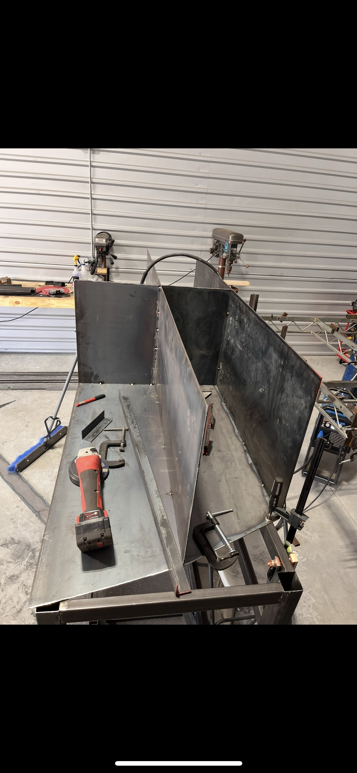 Metalwork in progress with sheet metal, power tools, and clamps on a workbench in a workshop.