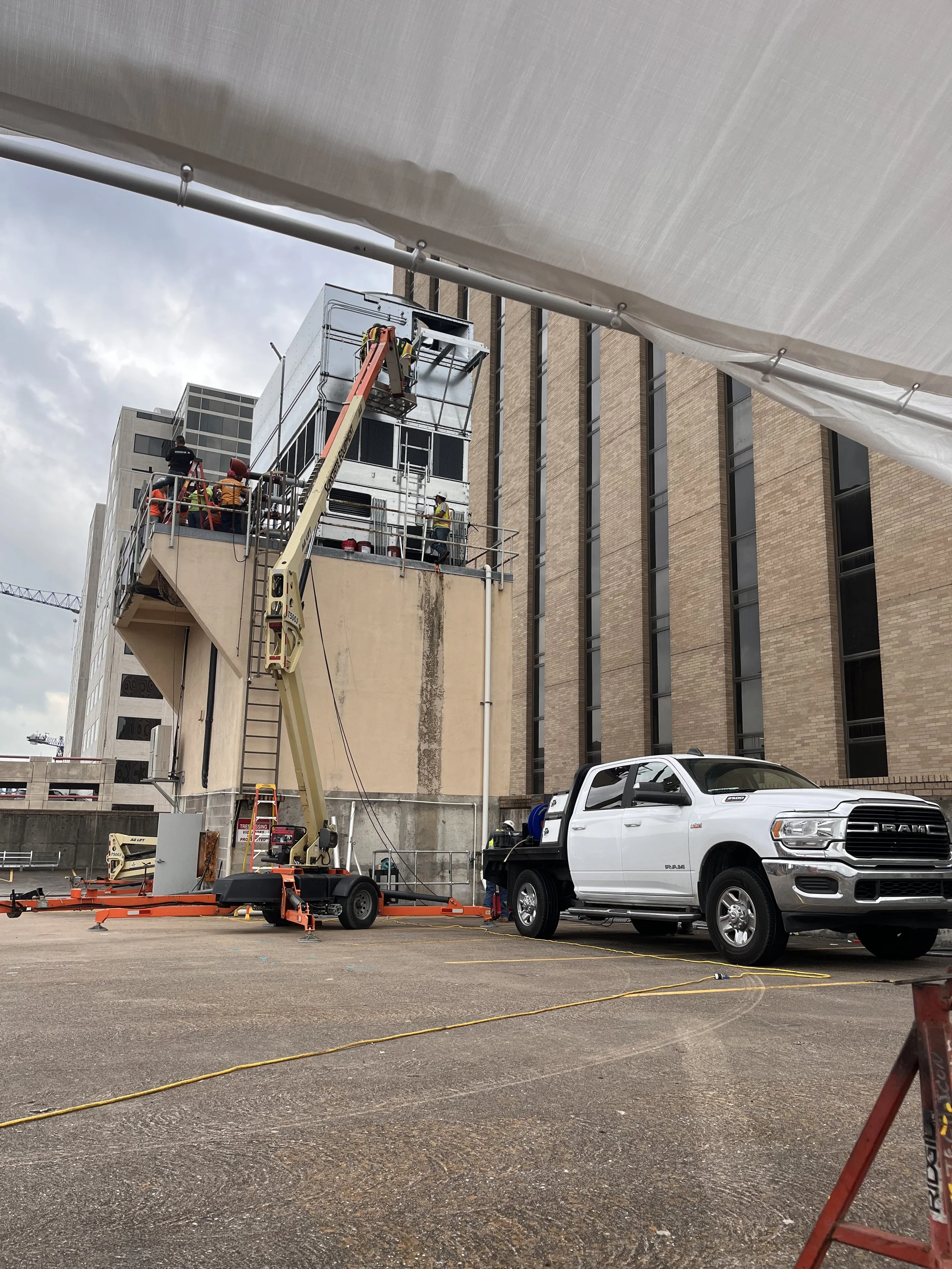 Construction workers on a lift working on the exterior of a brick building, with a white truck parked below and construction equipment in the foreground.