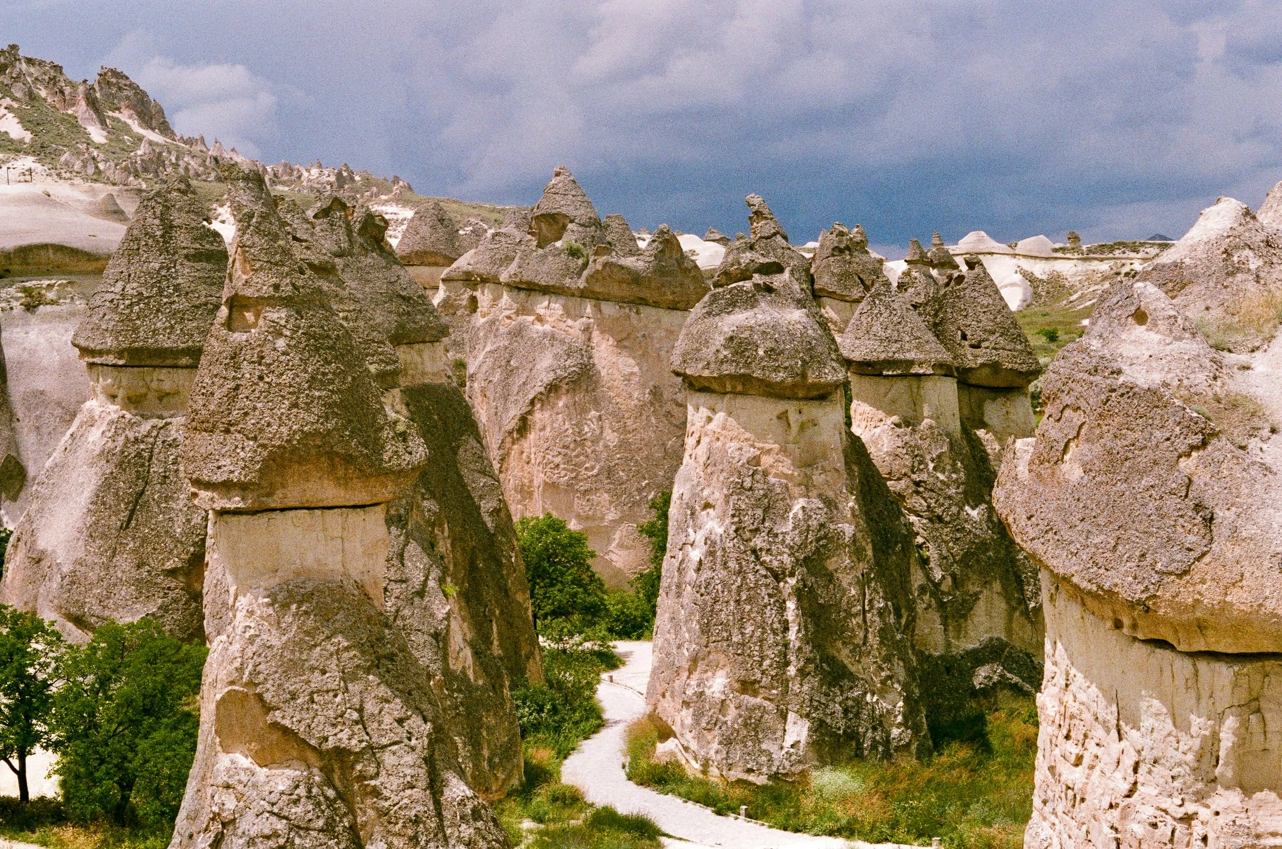 Unique rock formations in Cappadocia, Turkey, with a cloudy sky above and a small pathway at the base.