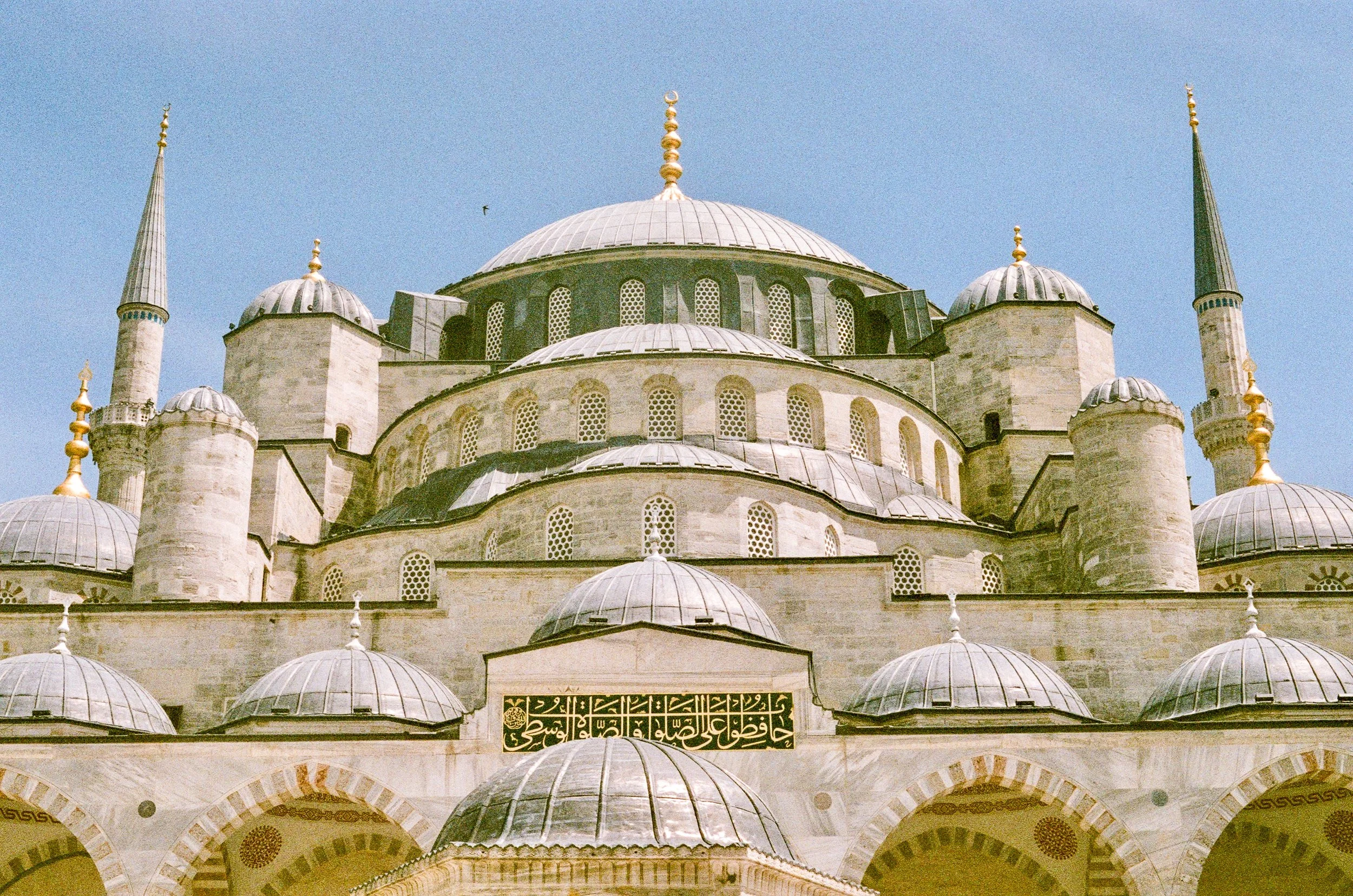 Close-up view of a mosque with multiple domes and minarets, featuring Arabic script on a decorative sign.