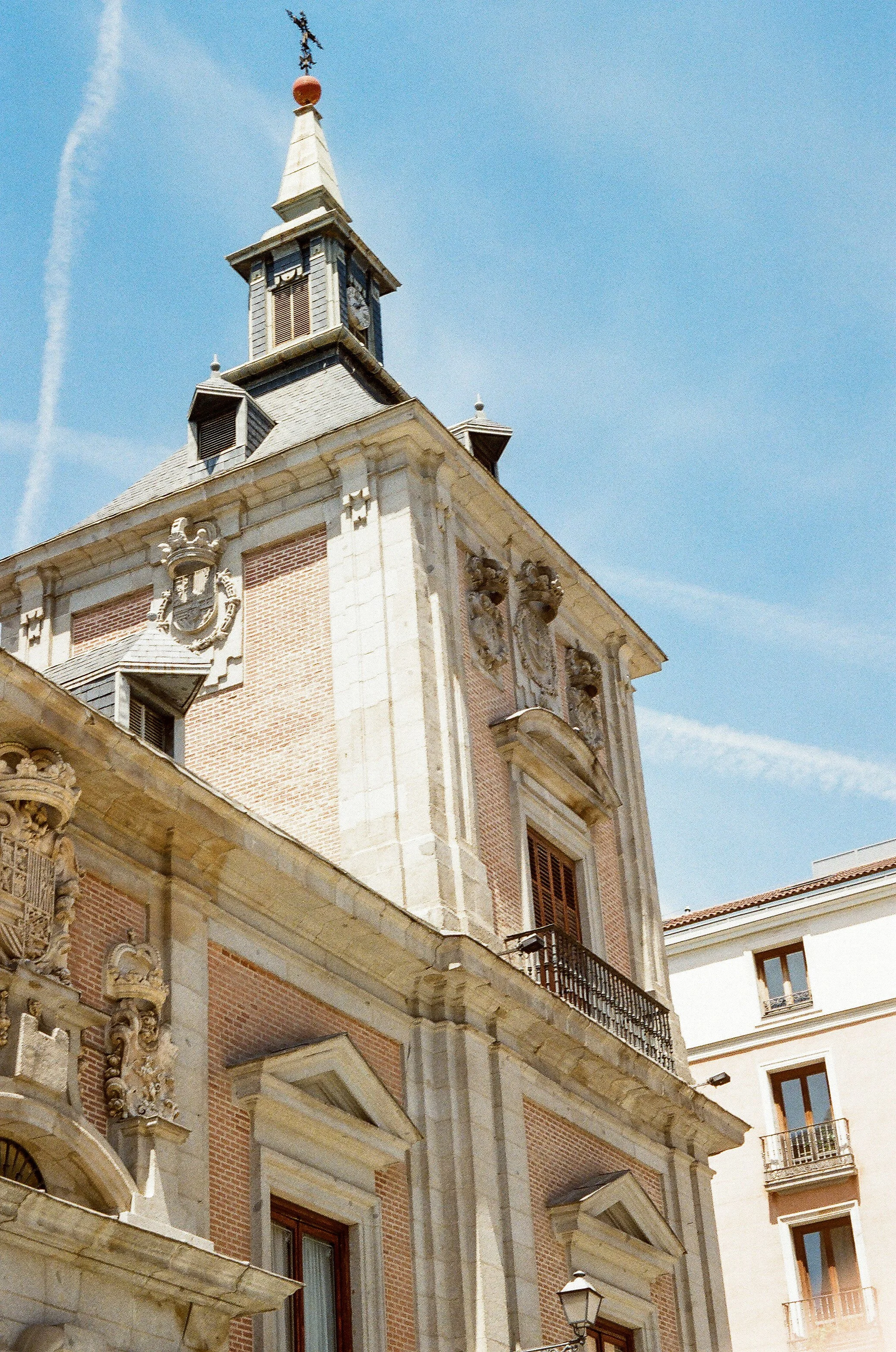 A historic building with ornate architecture, a clock tower, and a weather vane on top, set against a blue sky with a few clouds.