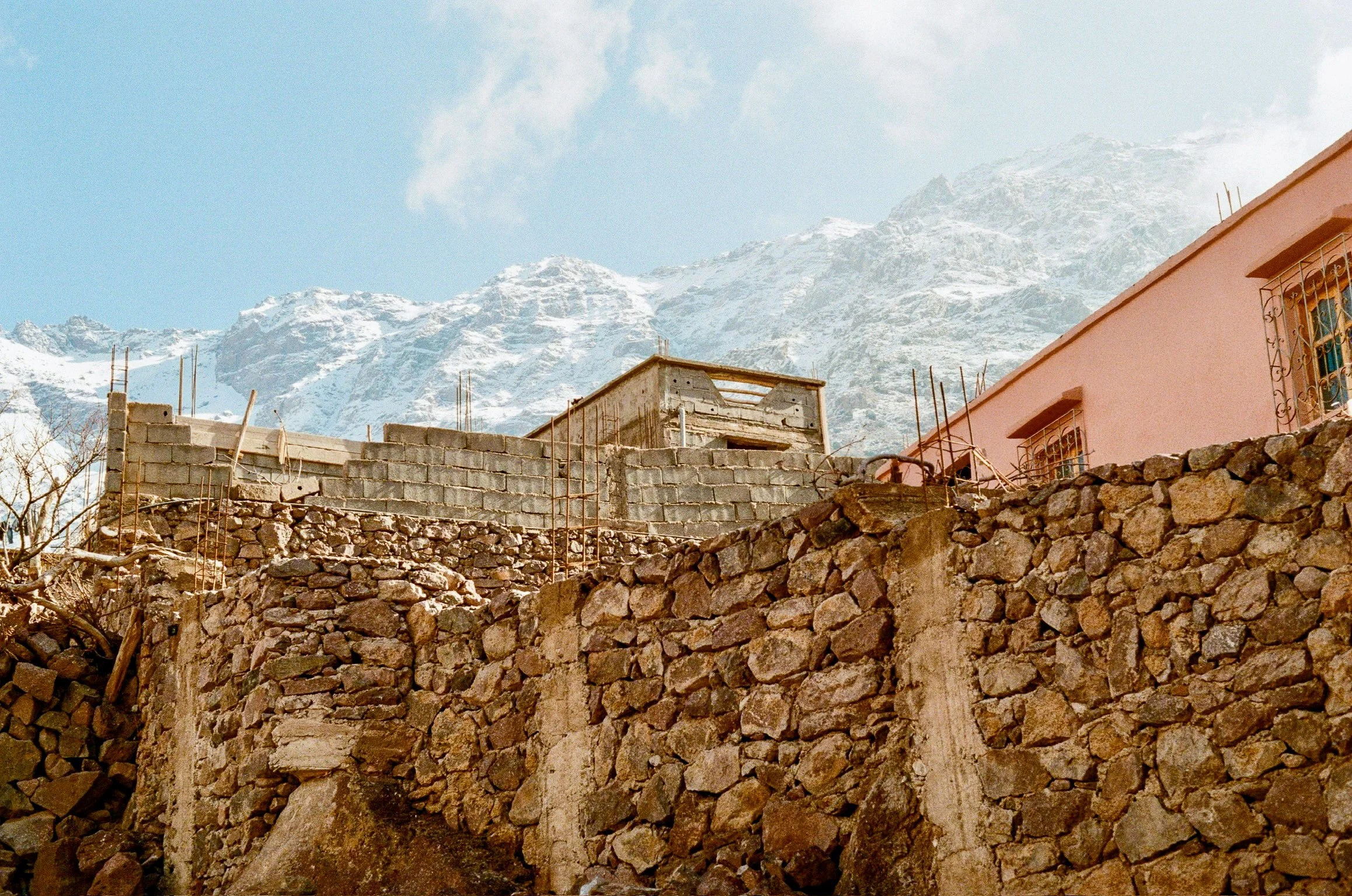 Mountains with snow and partially constructed buildings and stone walls in the foreground.