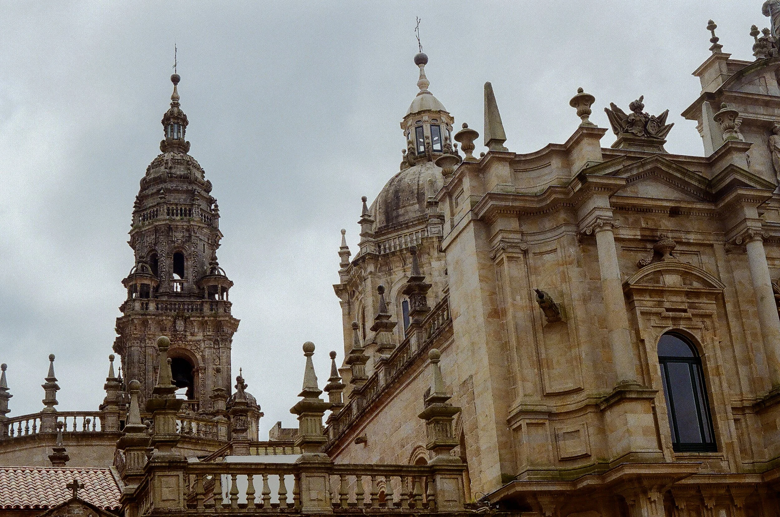 Close-up view of a historic cathedral's ornate stone facade with detailed carvings, spires, and a tower against a cloudy sky.