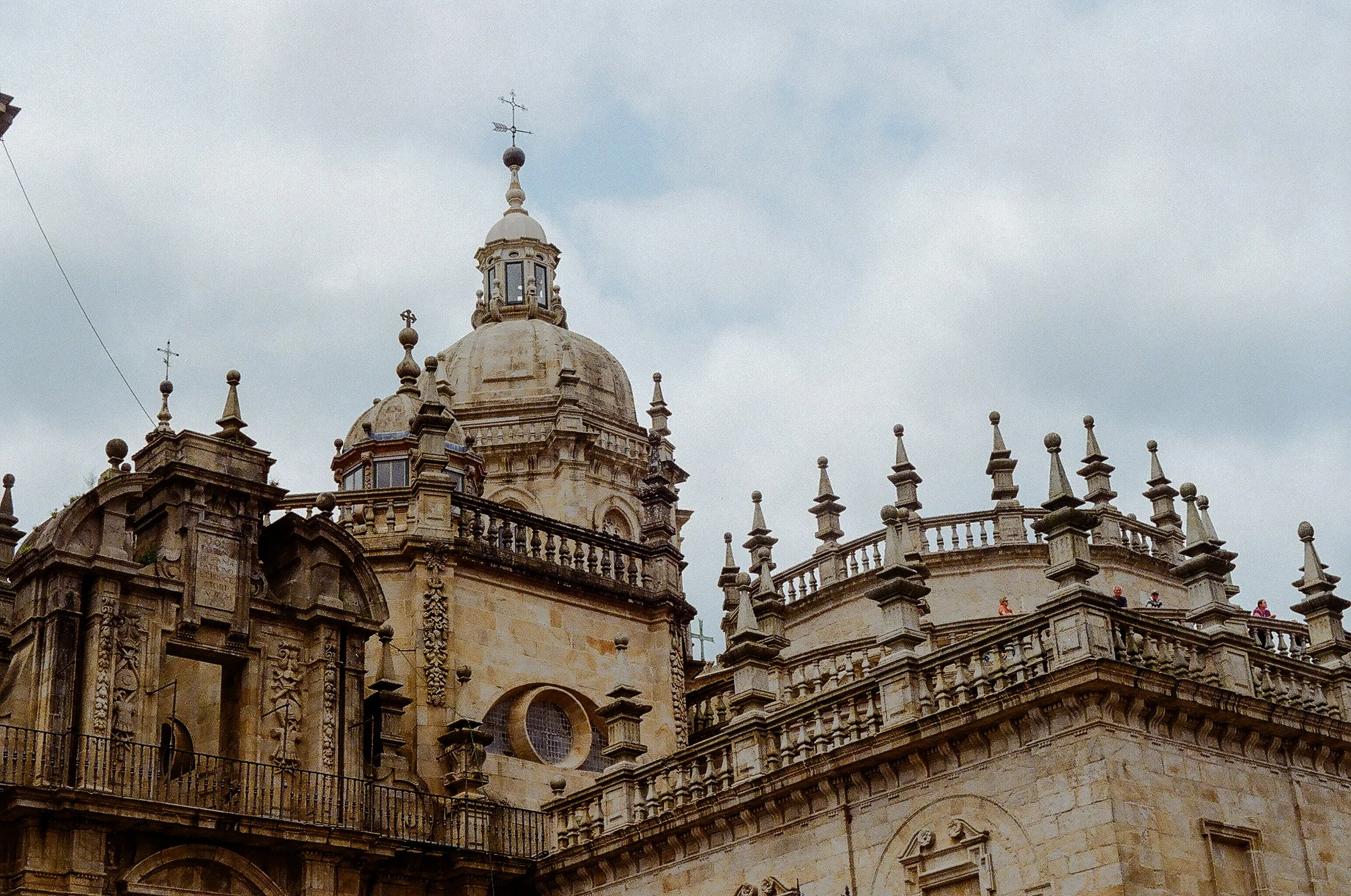 Historical stone building with ornate architecture, topped with a domed roof and weather vane, against a cloudy sky.