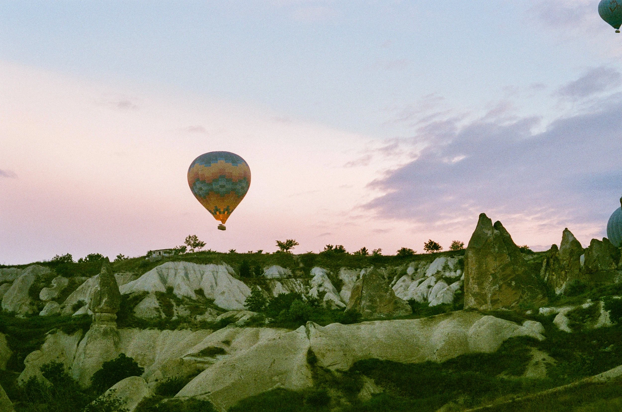 Hot air balloons flying over rocky landscape at dusk.