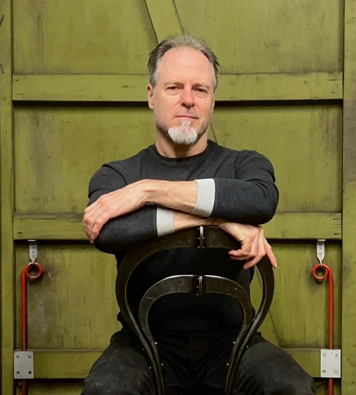 Portrait photo of artist Chris Shea sitting on a forged iron chair in his blacksmith studio