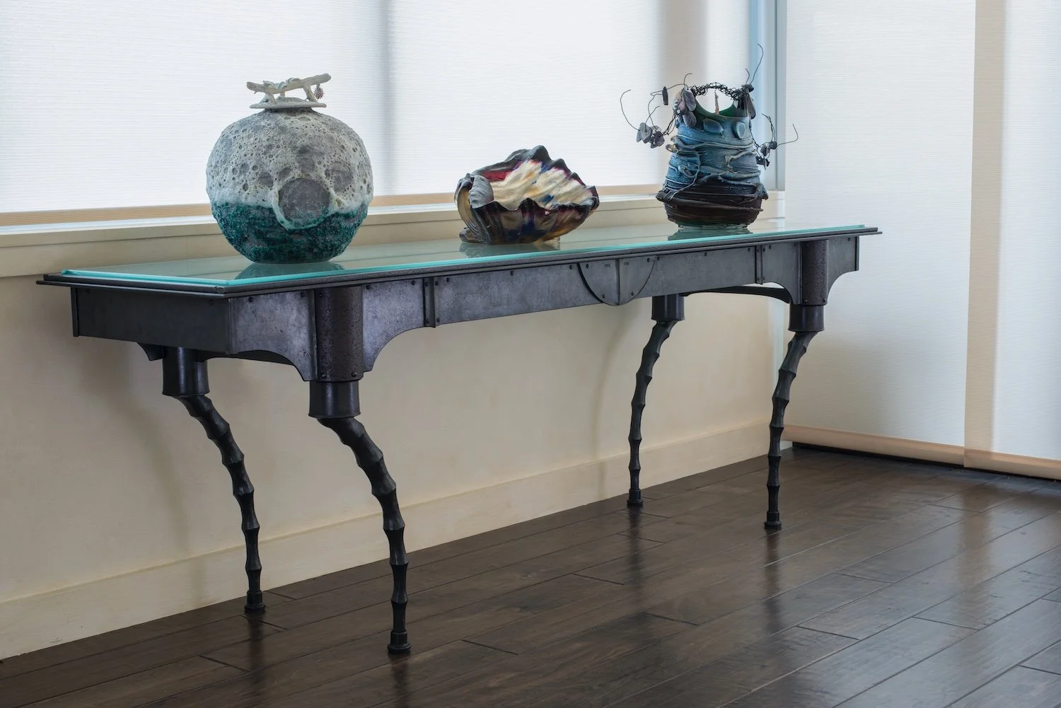 Hand forged iron console table with glass top and sculptural glass vessels on top