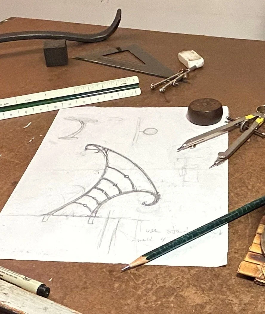 A sketch of a staircase plan on a piece of paper with drafting tools including a compass, ruler, square, and a marker on a wooden desk.