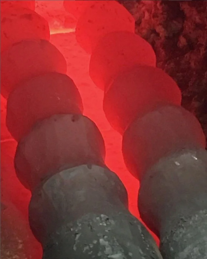 A close-up of a row of cylindrical pipes or barrels illuminated by a red light, viewed from above.
