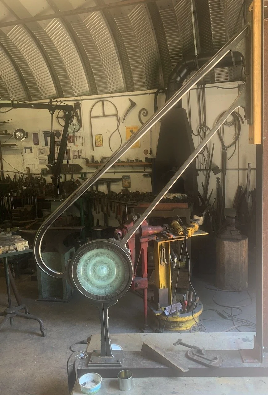 A forged iron handrail mounted to an armature in a blacksmith workshop, with a glass medallion inset into the railing design.