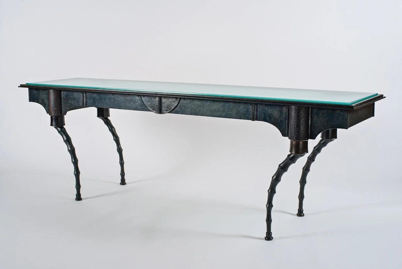 A vintage-style table with a light-colored top and ornate, curved black legs.