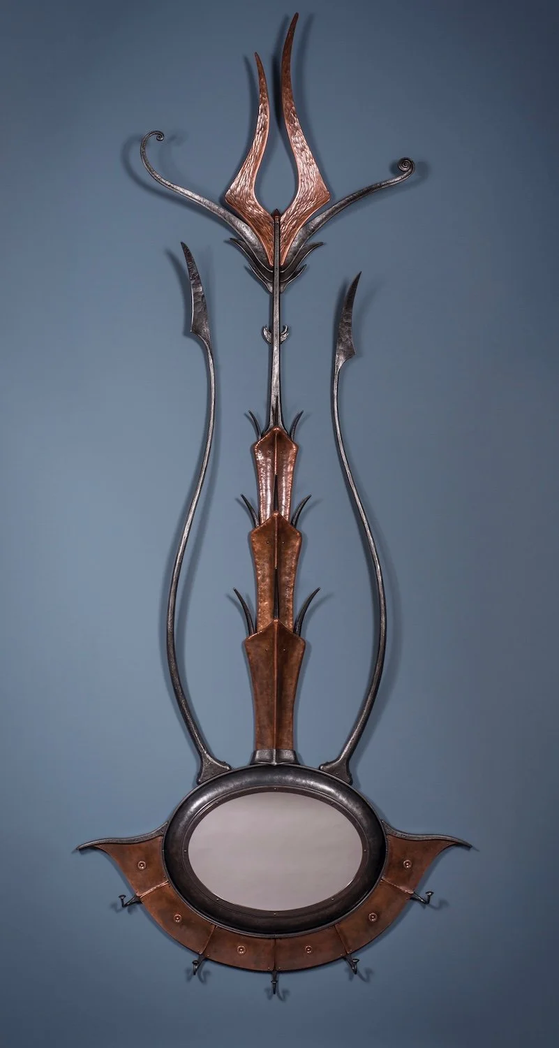 A decorative mirror with an ornate frame made of metal and wood, designed in an abstract, organic style with curved and pointed shapes resembling plant stems or creatures.