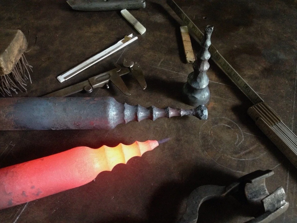 A workbench with various metal tools and objects, including a glowing hot metal piece, a ruler, and metal tongs.