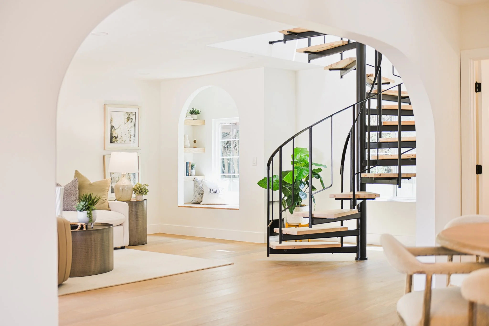 Interior view of a bright, modern living space with a spiral staircase, white walls, art pieces, and plants.