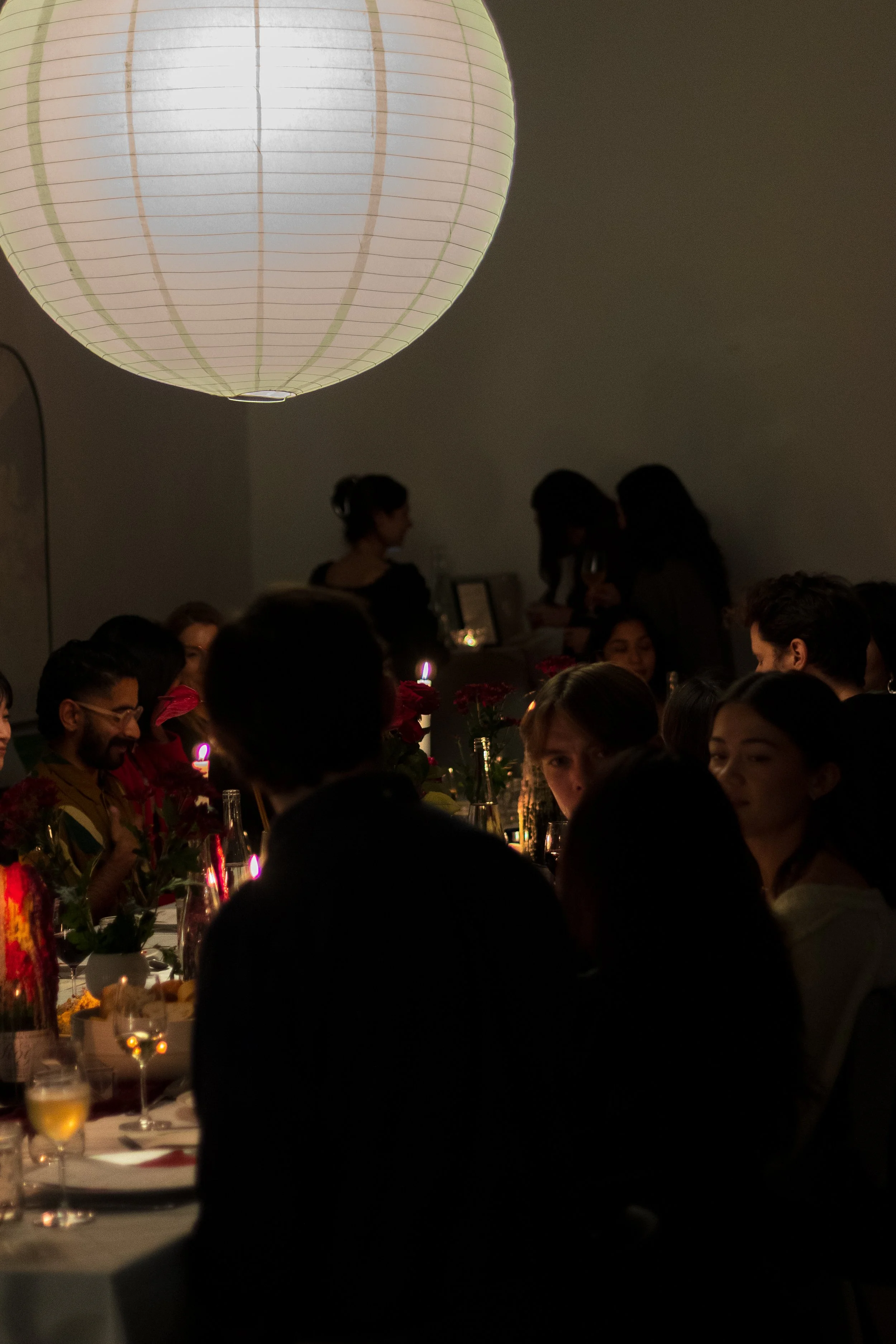 People gathered at a dinner party with a large paper lantern hanging from the ceiling.