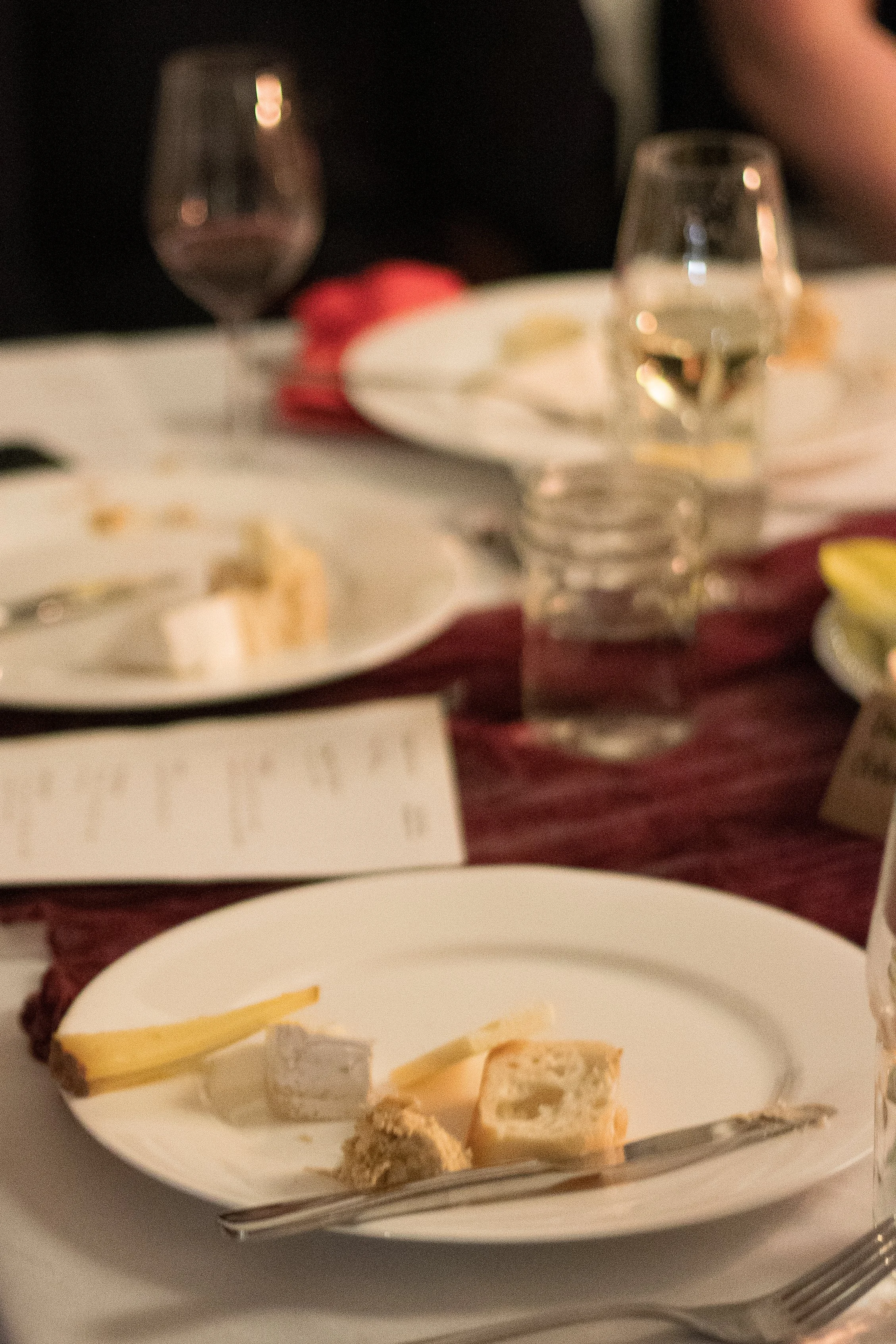 A table setting with a glass of water, a plate with a small piece of cheese and what appears to be a slice of bread, and a plate with assorted cheeses and crackers.