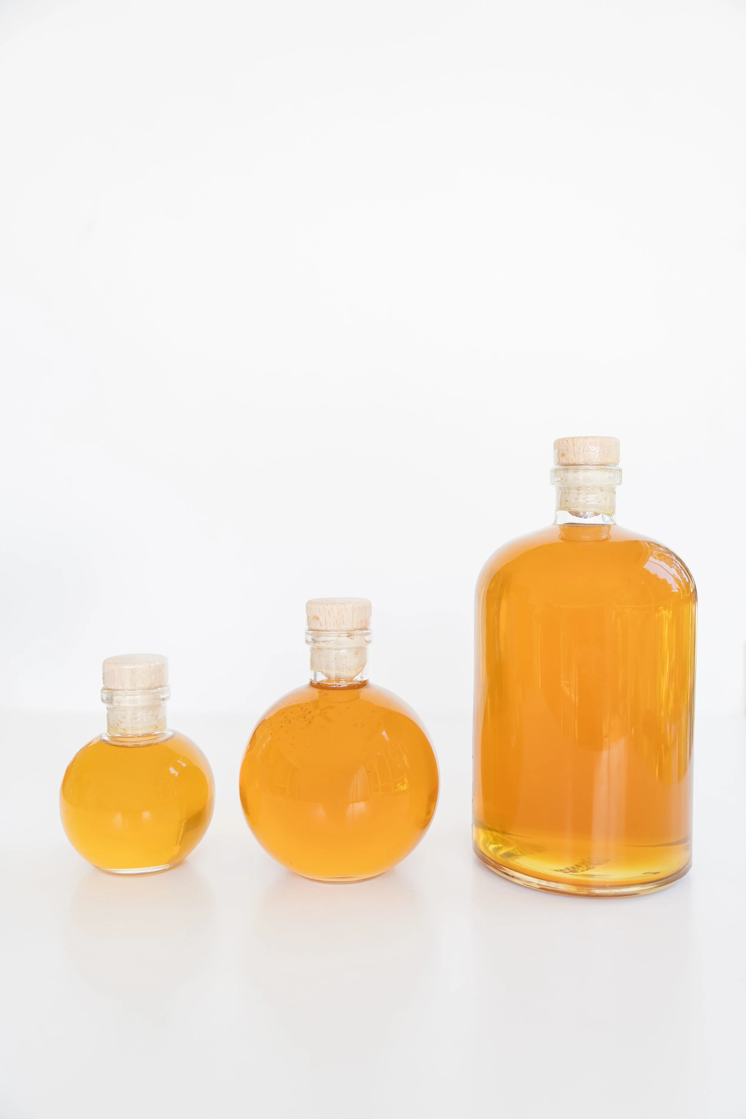 group of three different sizes of glass honey jars with corks against white background