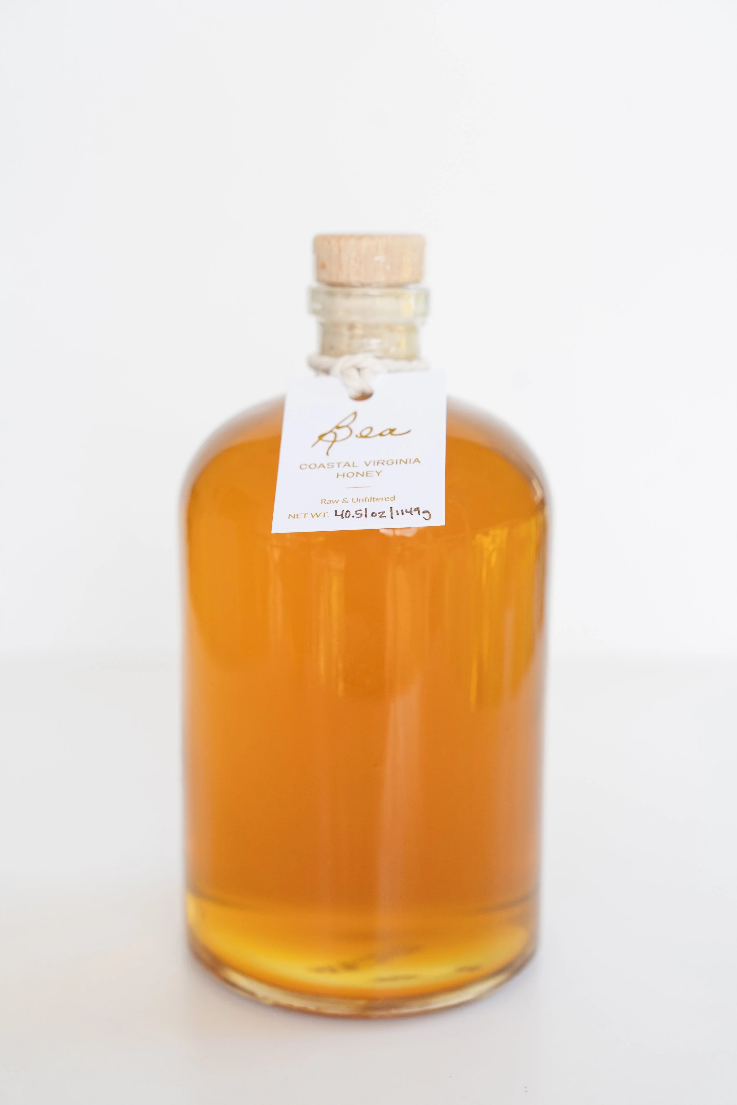 large glass jar of honey with cork top and hang tag