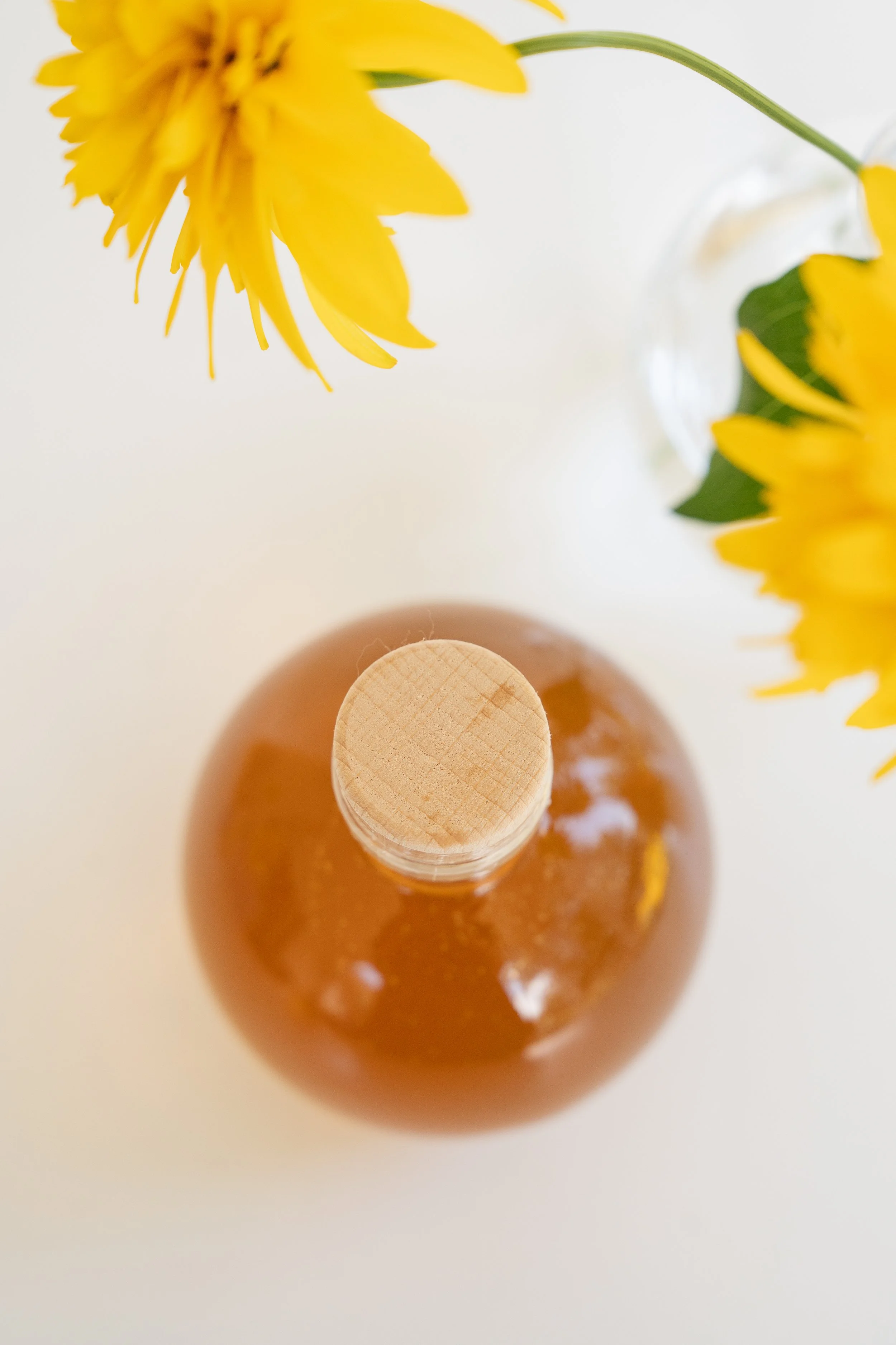 looking down on glass honey jar with cork and yellow flowers in corner