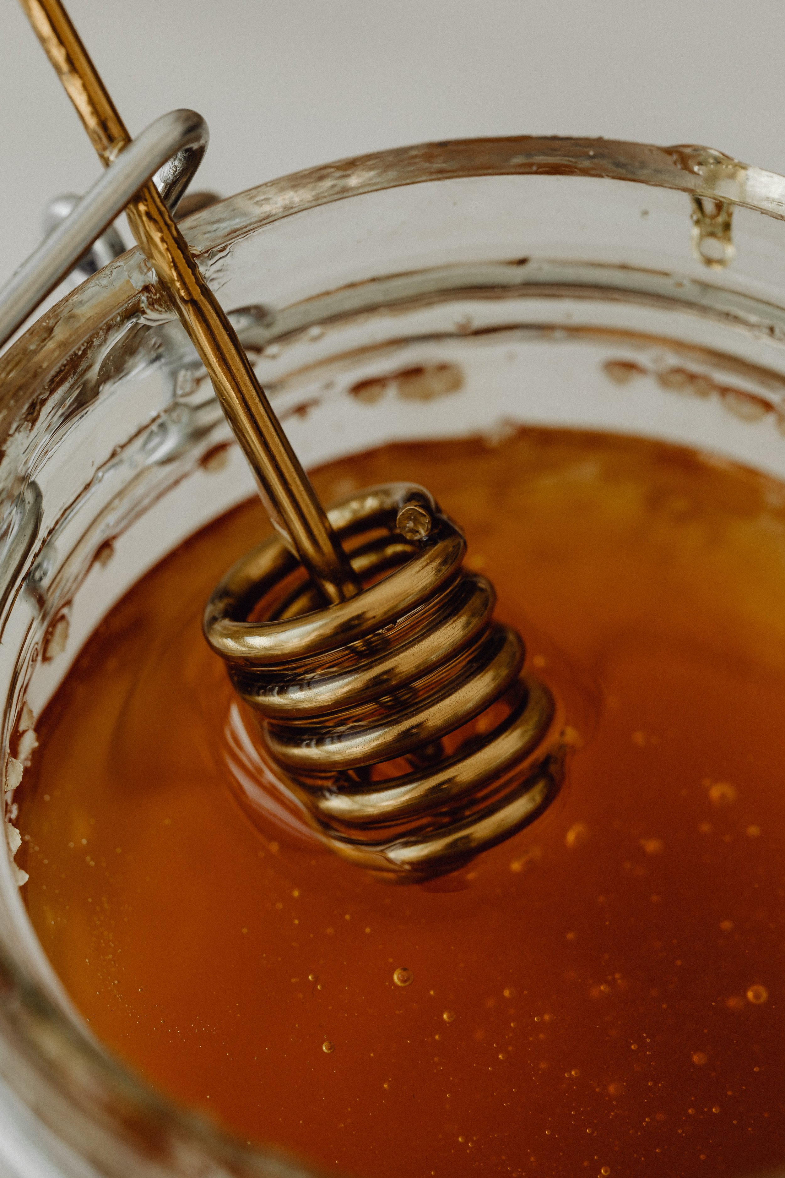 Close-up of a glass jar containing thick, amber-colored honey being stirred with a metal whisk