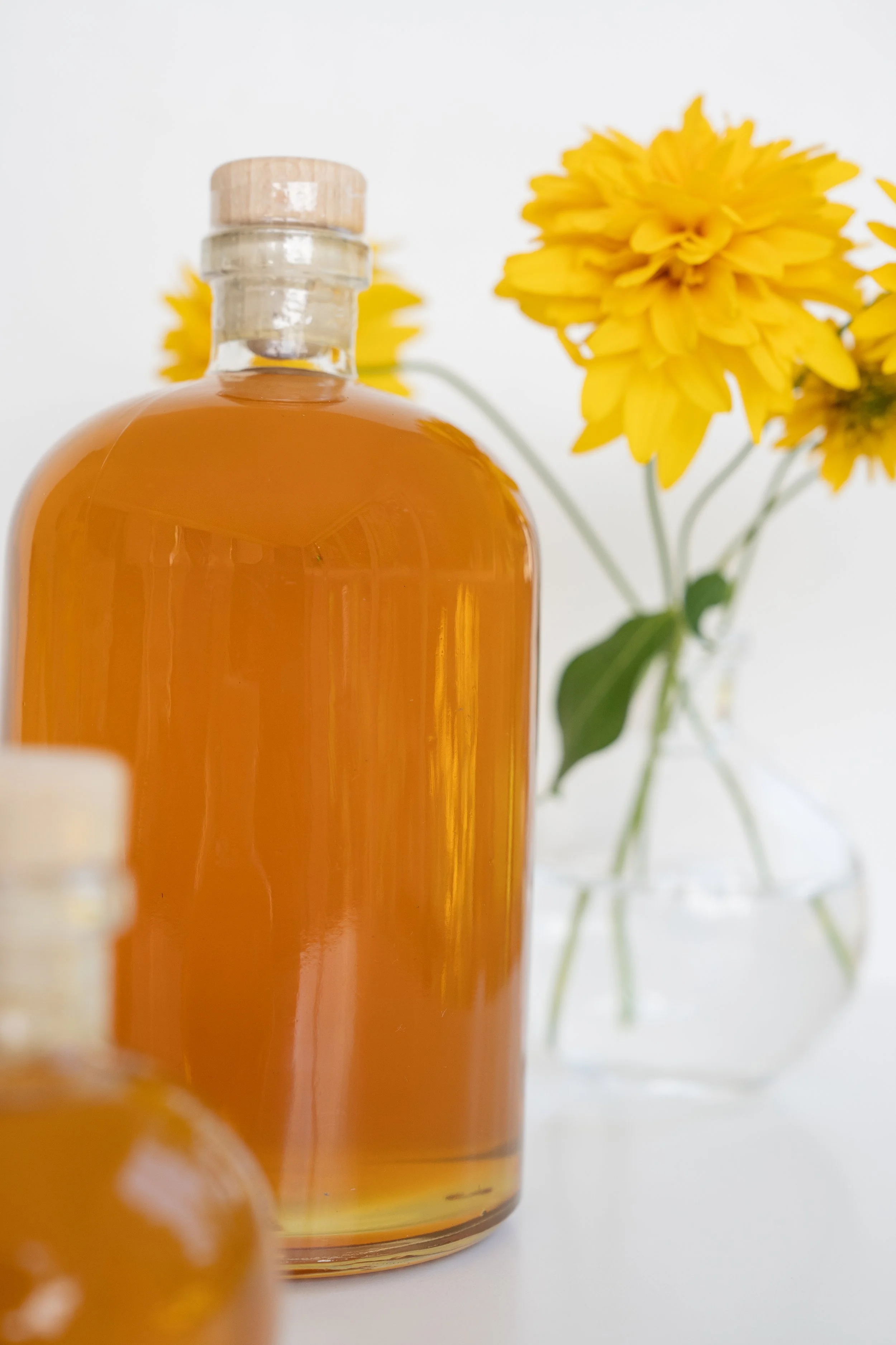 close up of large glass honey jar with yellow flowers in background